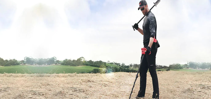 Détectoriste utilisant un détecteur de métaux Minelab Vanquish dans un champ, illustration d'un guide pratique sur les réglages, le balayage et l'interprétation des signaux.