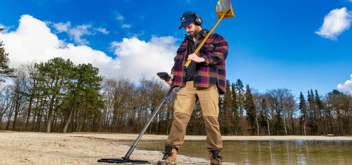 Détectoriste équipé d’un détecteur de métaux sur une plage de sable au bord de l’eau avec pelle de récupération pour la détection de loisirs.